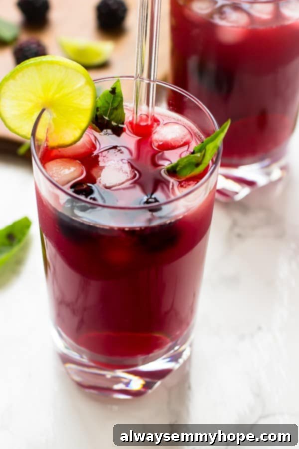 Close-up of a glass of blackberry limeade with a straw, showing the rich color and inviting texture.