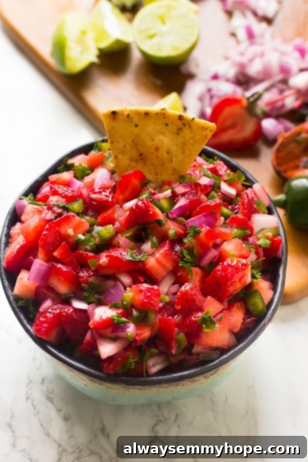 A top-down shot of strawberry jalapeno salsa in a bowl, with a tortilla chip dipped into it.