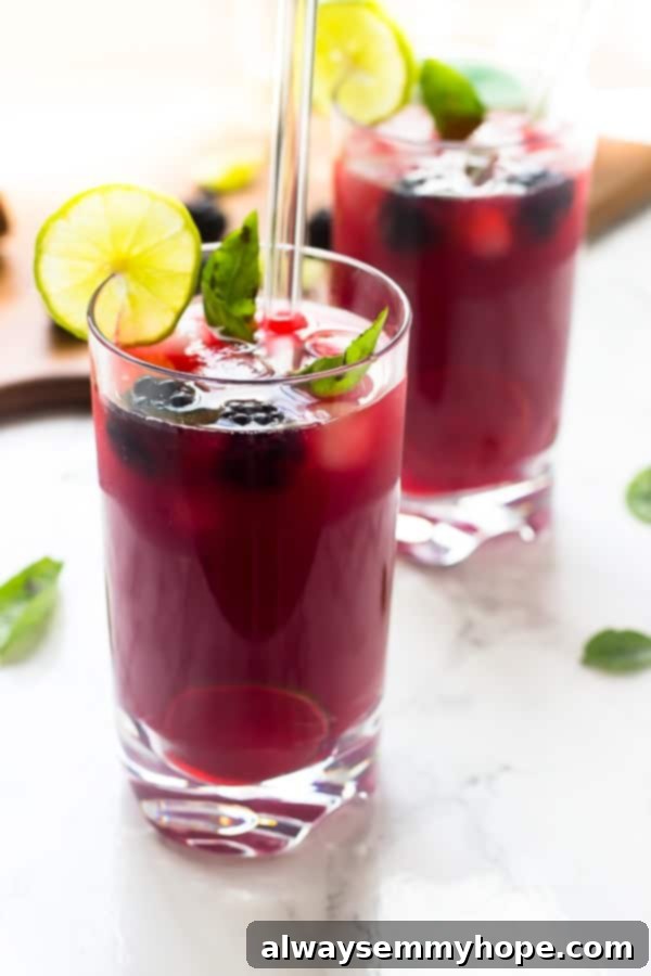 A side shot of two glasses of refreshing blackberry limeade on a rustic wooden table.