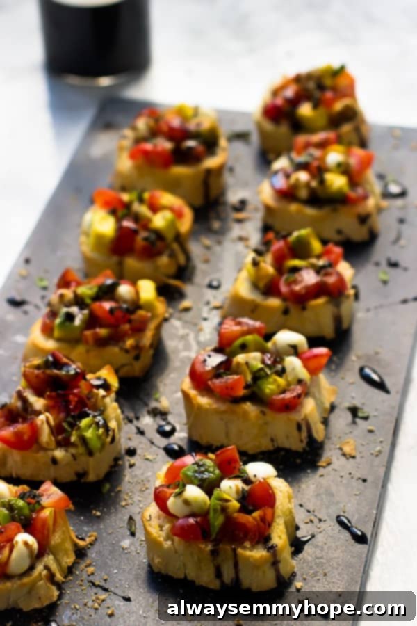 Blog Anniversary Special: 10 Minute Avocado Caprese Bruschetta 5 Rows of bruschetta drizzled with a balsamic reduction on a grey slate.