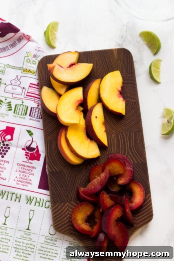 Overhead view of peach and plum slices on cutting board with lime wedges on counter