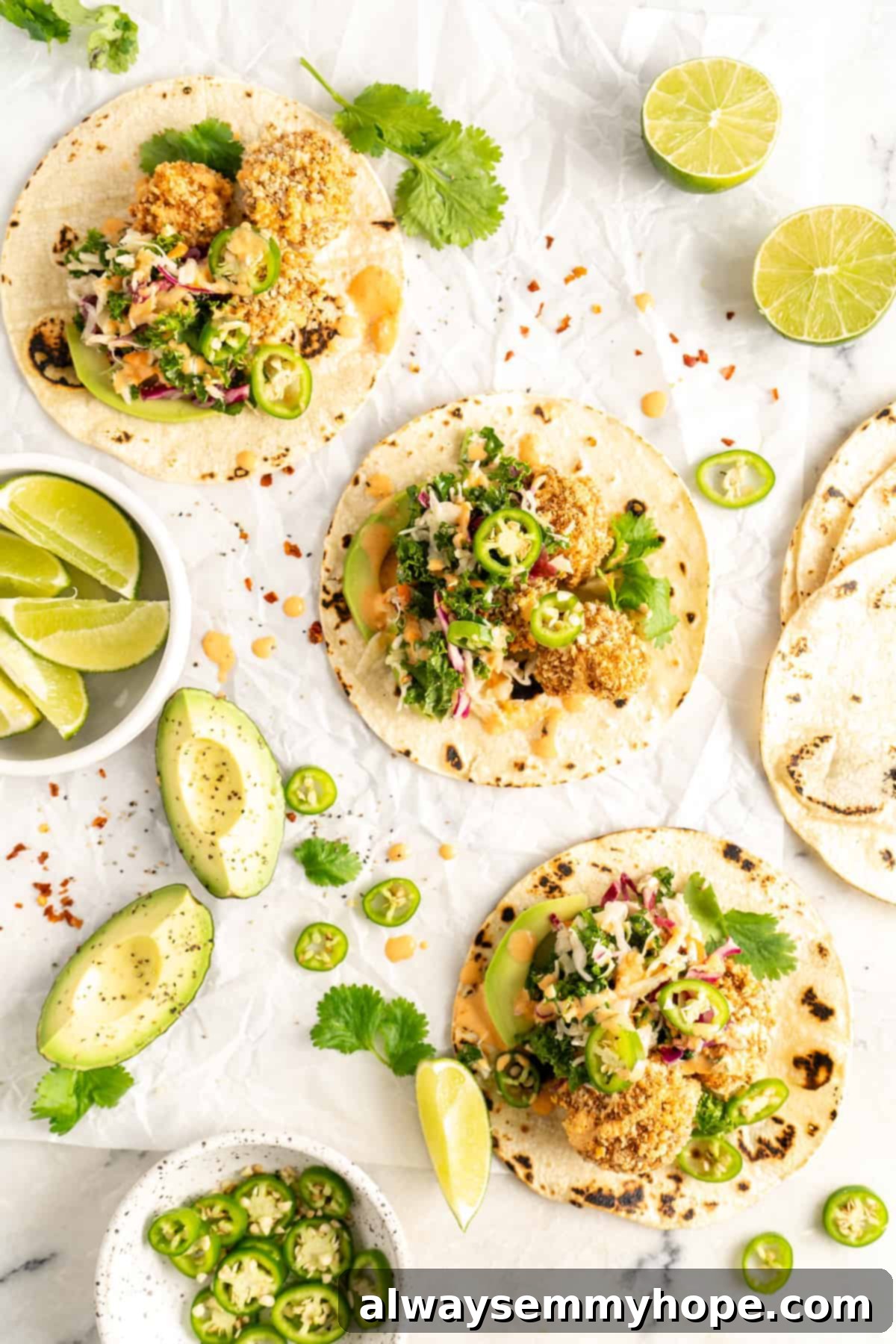 Crunchy Cauliflower Tacos with Smoky Chipotle Crema 9 Overhead view of several Crispy Cauliflower Tacos arranged beautifully with lime wedges, cilantro, and avocado slices as garnishes