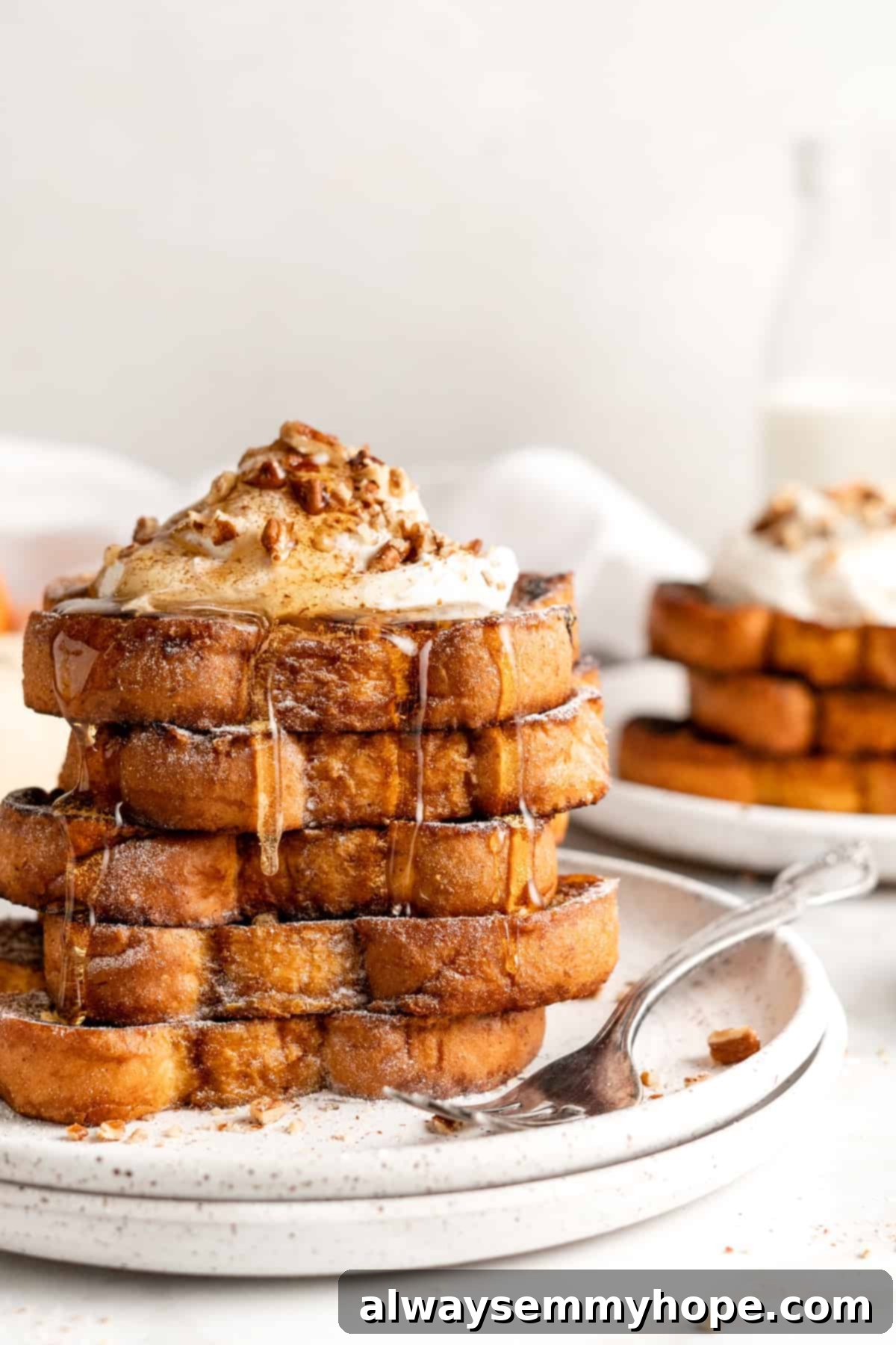 Two plates with stacks of pumpkin French toast topped with syrup, whipped cream, and nuts