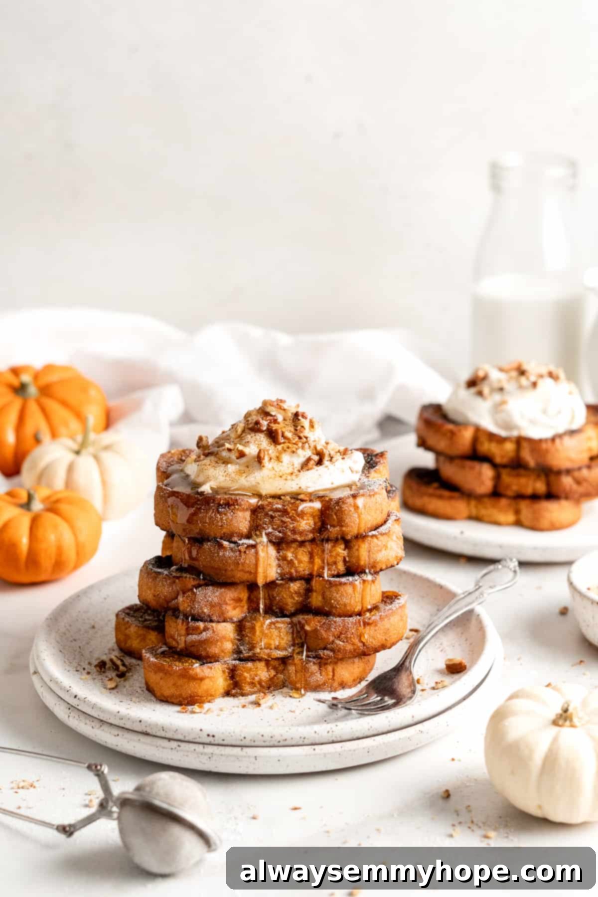 Two plates with stacks of pumpkin French toast garnished with whipped cream and nuts