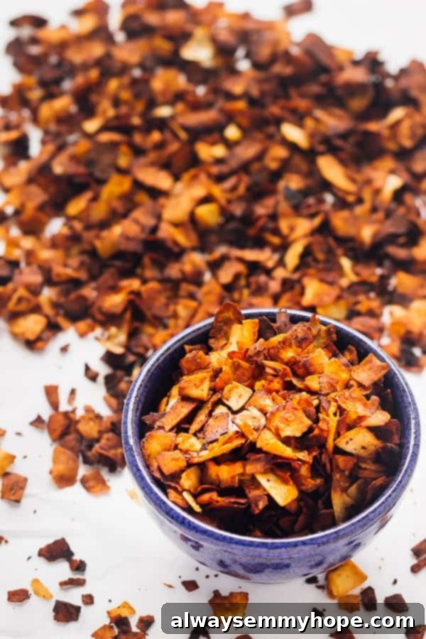 These gluten-free vegan bacon crumbles are made out of coconut, and taste just like real bacon. They're salty, smoky, and sweet! A blue bowl brimming with golden-brown coconut bacon crumbles, with a larger pile of the crispy vegan bacon in the soft-focused background.