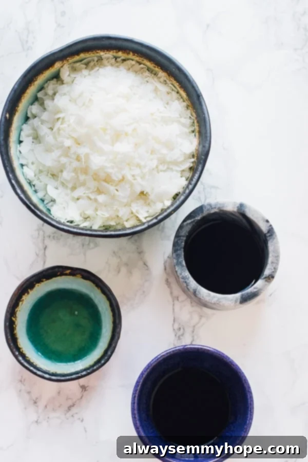 These gluten-free vegan bacon crumbles are made out of coconut, and taste just like real bacon. They're salty, smoky, and sweet! An overhead shot showcasing the key ingredients for vegan bacon crumbles: a bowl of vibrant white coconut flakes, a small bowl of dark tamari, a tiny bottle of liquid smoke, and a golden pool of maple syrup.