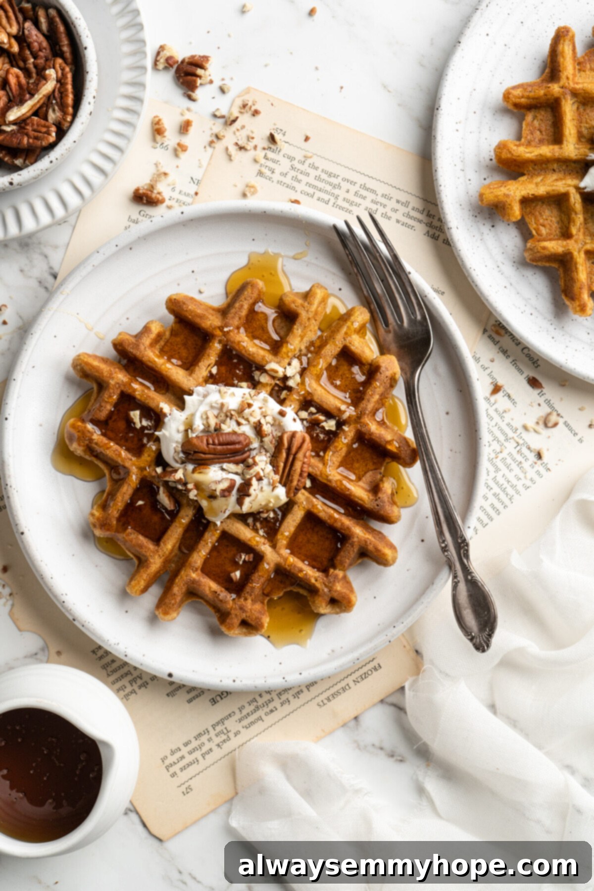 These easy vegan pumpkin waffles are light, fluffy, and crispy, with your favorite fall flavors, and can easily be made gluten-free. Overhead view of a plate with a fork, a pumpkin waffle, a dollop of whipped coconut cream, and candied pecans, next to a plate with another waffle