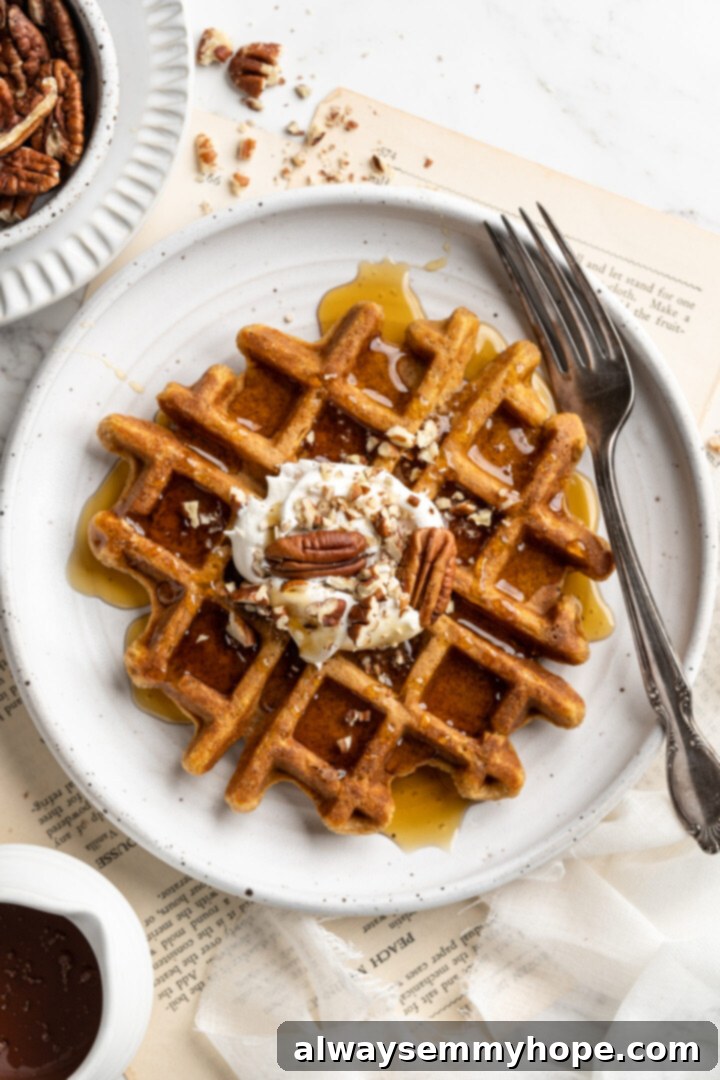 These easy vegan pumpkin waffles are light, fluffy, and crispy, with your favorite fall flavors, and can easily be made gluten-free. Overhead view of a pumpkin waffle on a plate with a fork, topped with coconut cream and pecans