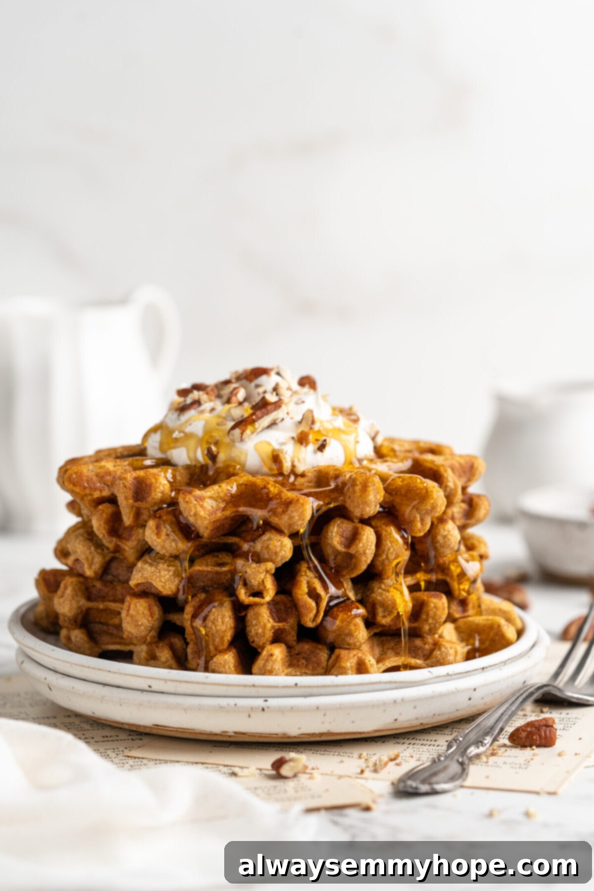 These easy vegan pumpkin waffles are light, fluffy, and crispy, with your favorite fall flavors, and can easily be made gluten-free. A stack of pumpkin waffles topped with coconut cream and candied pecans