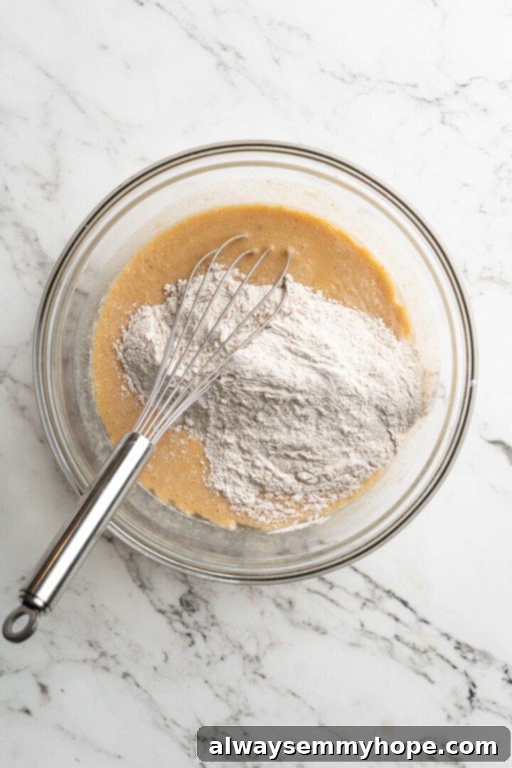 These easy vegan pumpkin waffles are light, fluffy, and crispy, with your favorite fall flavors, and can easily be made gluten-free. A mixing bowl with a pile of flower on top of wet ingredients, with a whisk