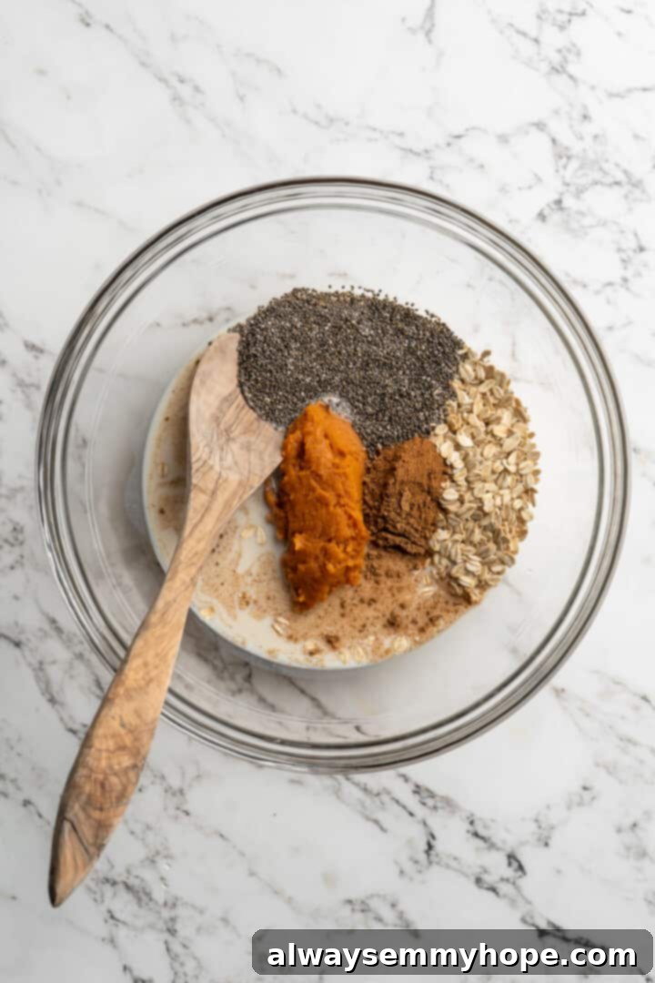 ingredients for overnight oats in a glass bowl with a wooden spoon, ready to be mixed