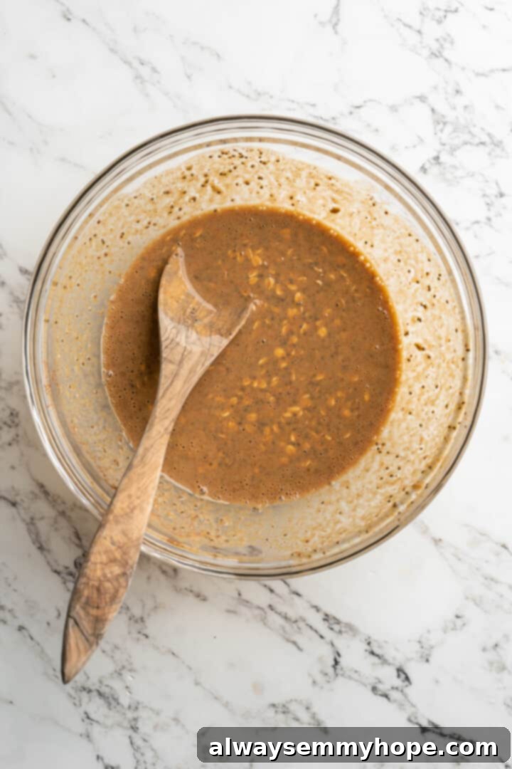 mixed ingredients in glass bowl with wooden spoon, showing the creamy pumpkin oat mixture