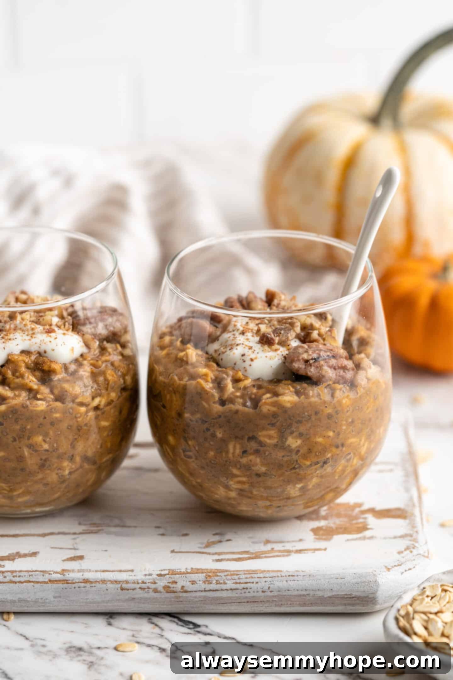 two jars of pumpkin pie overnight oats with spoon inside one and pumpkins in background 45 degree angle, showcasing a beautiful fall breakfast