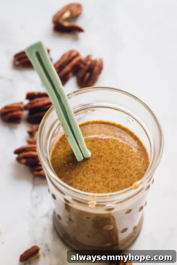 Homemade Pecan Butter: Quick & Easy 4-Ingredient Recipe A glass jar filled with freshly made homemade pecan butter, with a spoon resting in it, against a rustic background.