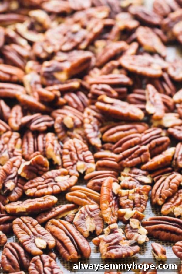 Toasting Pecans for Homemade Nut Butter Freshly toasted pecans spread evenly on a silicone baking mat on a baking sheet, steam gently rising.