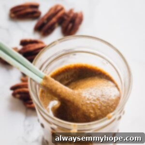 Pecan Butter from Scratch 2 A spoon scooping out creamy pecan butter from a transparent glass jar, ready to be enjoyed.