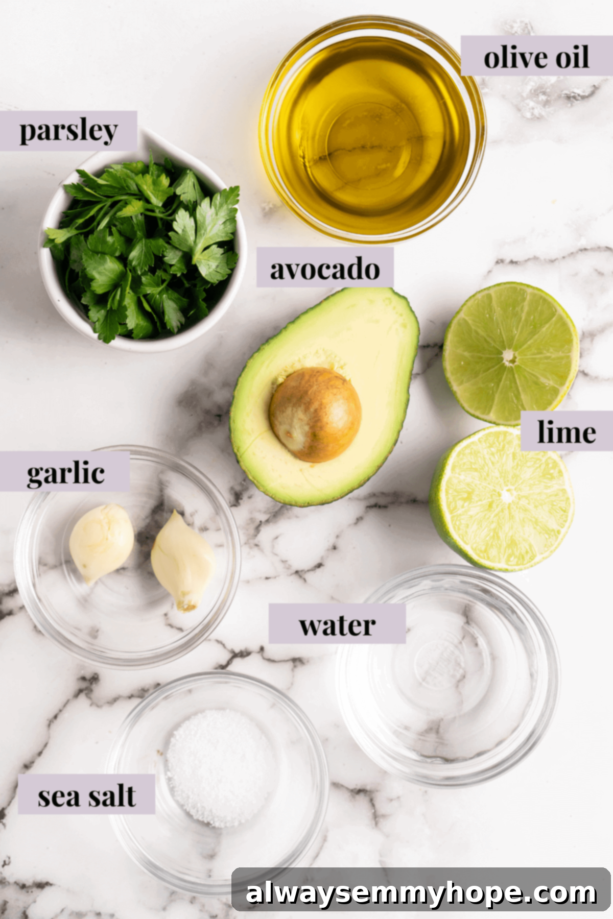Naturally Creamy Vegan Avocado Dressing 3 Overhead view of fresh ingredients for creamy vegan avocado dressing including a halved avocado, lime, garlic cloves, and fresh herbs, arranged on a rustic wooden cutting board.