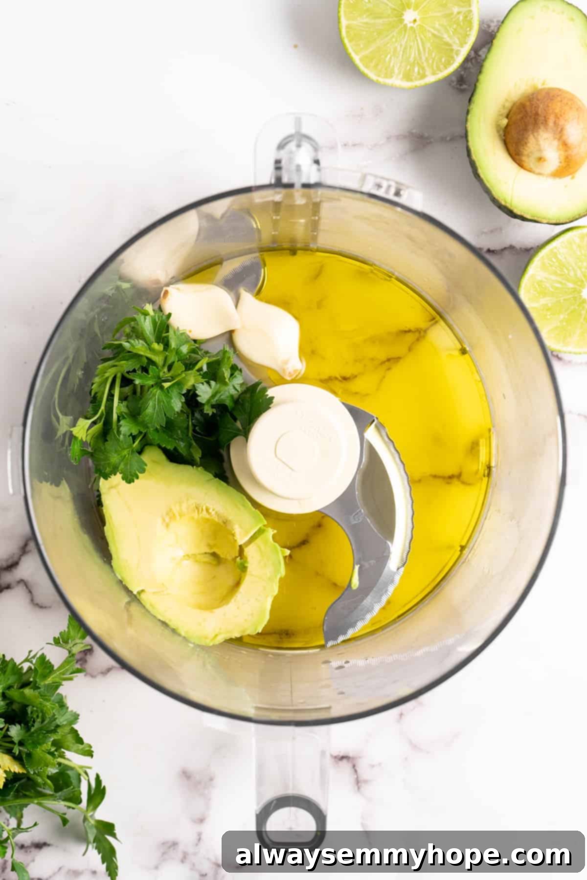Naturally Creamy Vegan Avocado Dressing 4 All creamy vegan avocado dressing ingredients including half an avocado, fresh herbs, lime, garlic, and olive oil, precisely placed in a food processor, ready for blending.