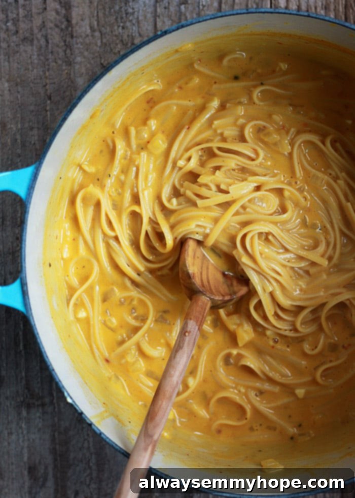 Quick Fall Vegan Dinners: 25 Recipes Ready in 15 Minutes 18 Wooden spoon stirring creamy pumpkin pasta in a blue pot.