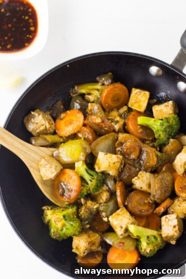 Overhead shot of a delicious tofu and broccoli stir fry in a black skillet, glistening with a savory sauce.