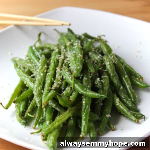 A pile of savory garlic parmesan sesame stir-fry green beans on a square white plate, glistening with seasoning.
