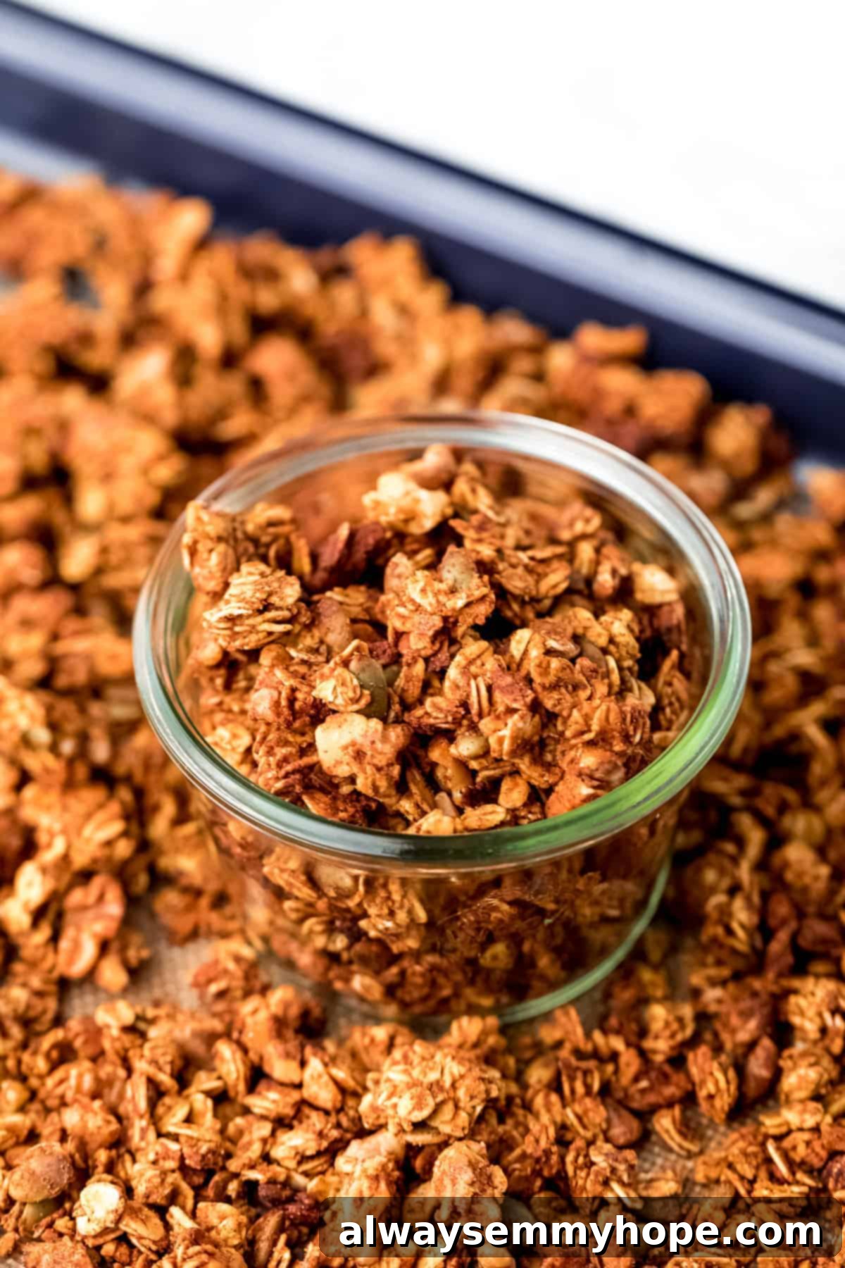 A glass jar filled with golden pumpkin granola, surrounded by loose granola on a baking sheet, ready for storage or serving.