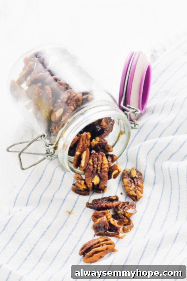Jar of candied pecans spilling onto kitchen towel, highlighting the homemade charm and delicious appeal.