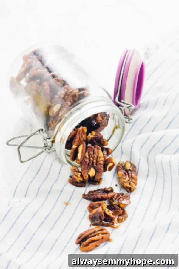 A glass jar filled to the brim with homemade candied pecans, with some spilling onto a rustic kitchen towel, highlighting their appealing texture.
