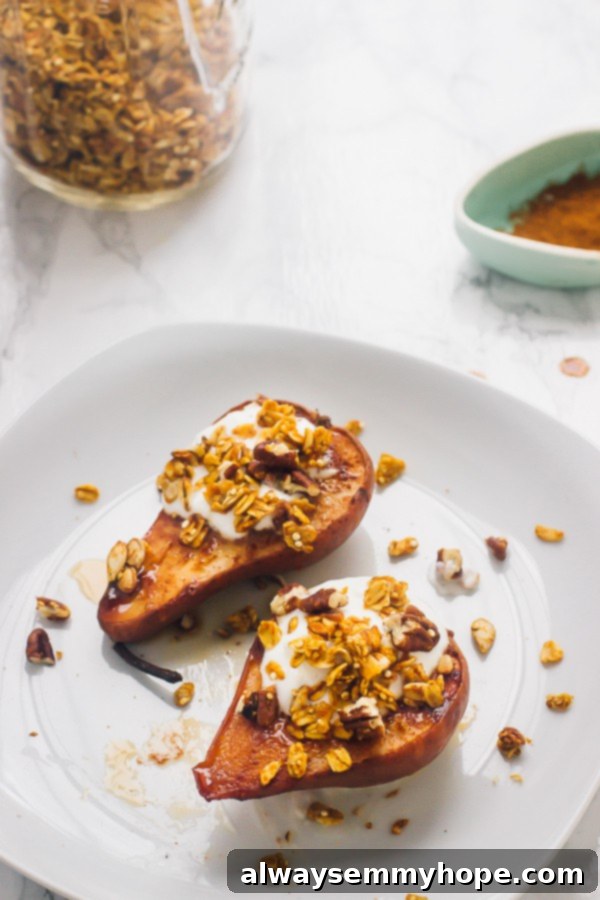 Top-down view of two beautifully baked cinnamon pear halves, garnished with crunchy granola and a drizzle of coconut cream on a clean white plate.