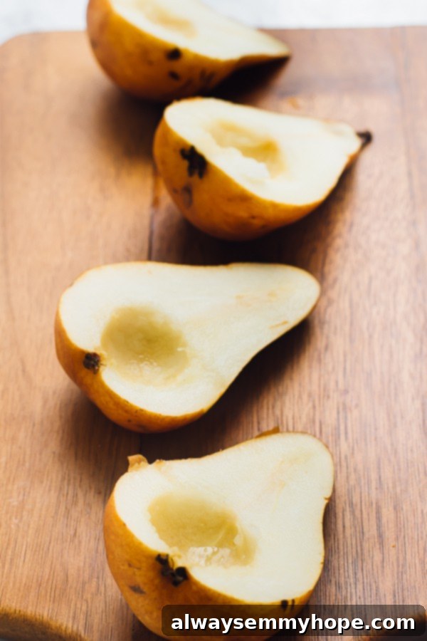 Four fresh pear halves arranged neatly on a rustic wooden chopping board, showing their crisp texture before baking.