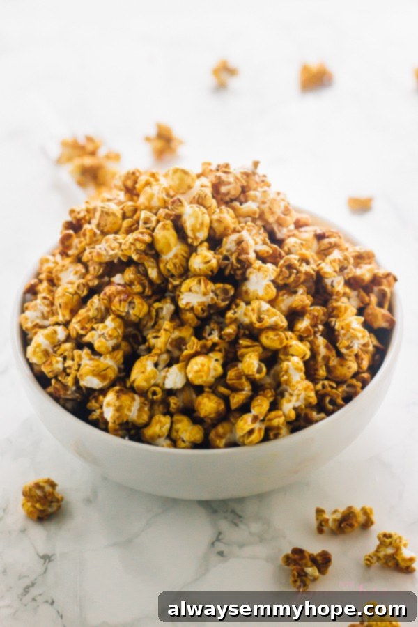 This easy vegan caramel popcorn recipe is the perfect sweet and salty snack. No corn syrup needed, and it comes together in 25 minutes! A bowl full of caramel corn with pieces on the table around it, highlighting its golden, crunchy texture.