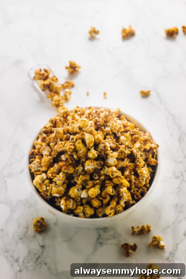 This easy vegan caramel popcorn recipe is the perfect sweet and salty snack. No corn syrup needed, and it comes together in 25 minutes! Overhead view of a bowl full of caramel popcorn on a marble surface, with pieces of caramel corn around it, perfectly arranged.