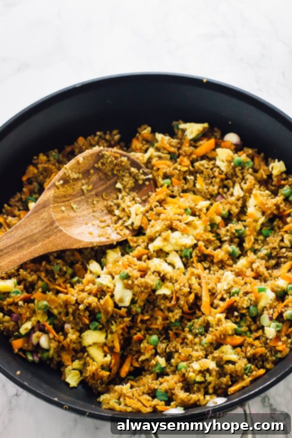 Speedy 15 Minute Quinoa Fried Rice 3 Quinoa fried rice being stirred with a wooden spoon in a black skillet, showcasing the cooking process.
