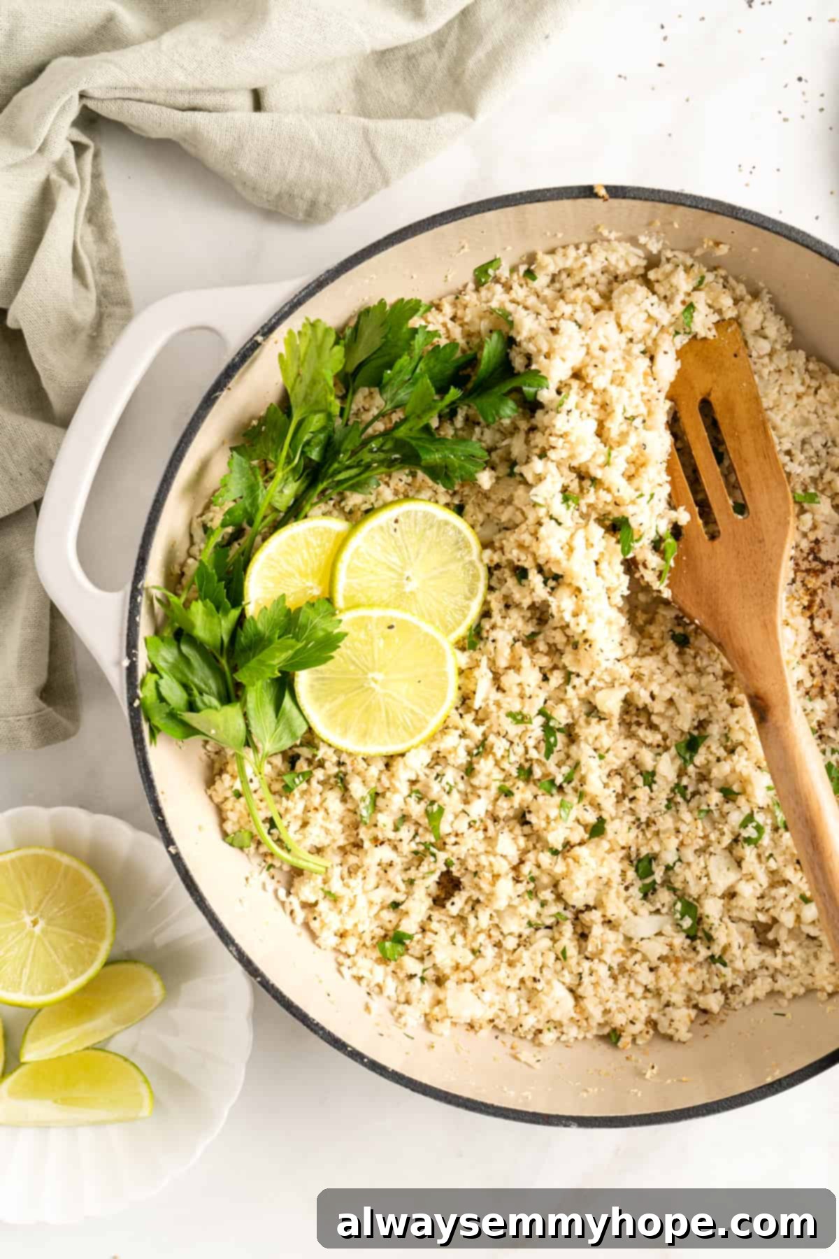 Overhead view of perfectly cooked cauliflower rice in a skillet, garnished with fresh parsley sprigs and vibrant lime slices