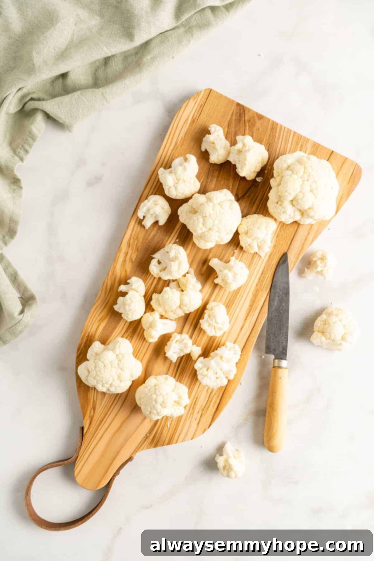 Overhead view of a head of cauliflower on a wooden cutting board, with a knife poised to cut it into florets.