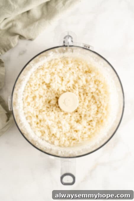 Overhead view of cauliflower rice after being pulsed in a food processor, resembling tiny grains.