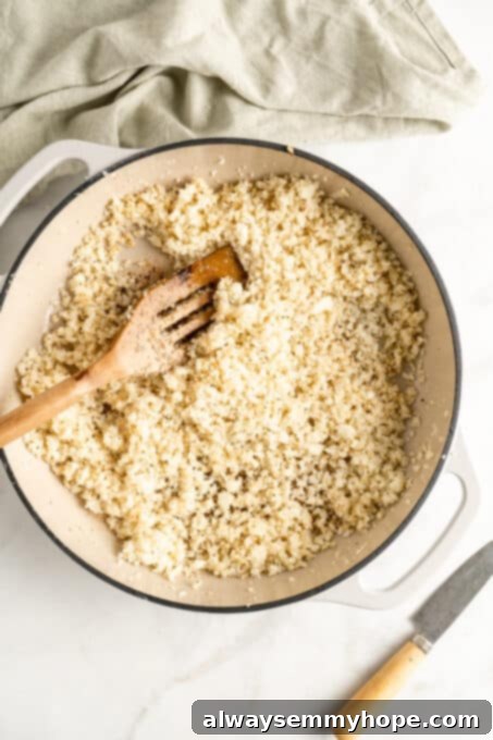 Overhead view of cooked cauliflower rice in a cast iron skillet, perfectly browned and seasoned, with a wooden spatula resting in it.