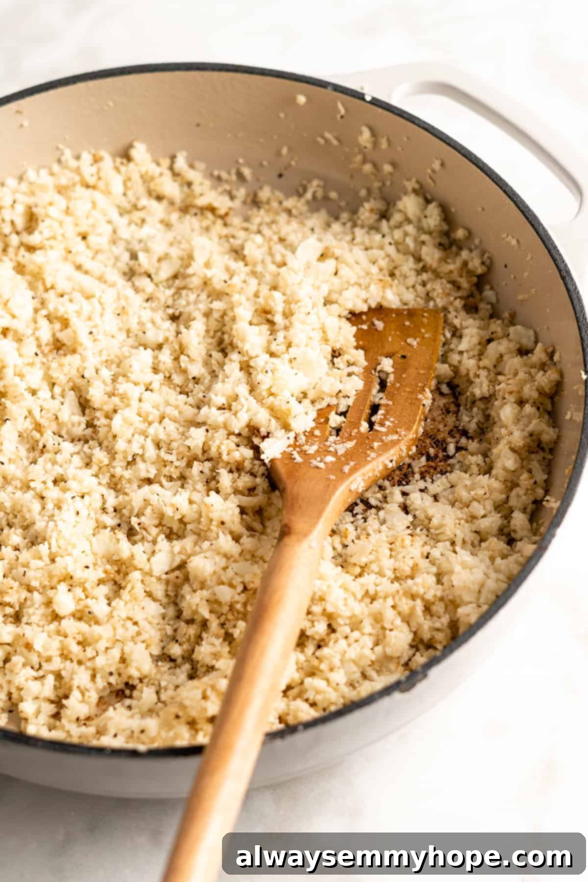 Cooked cauliflower rice, beautifully browned and seasoned, resting in a cast iron skillet with a wooden spatula, ready to be served.