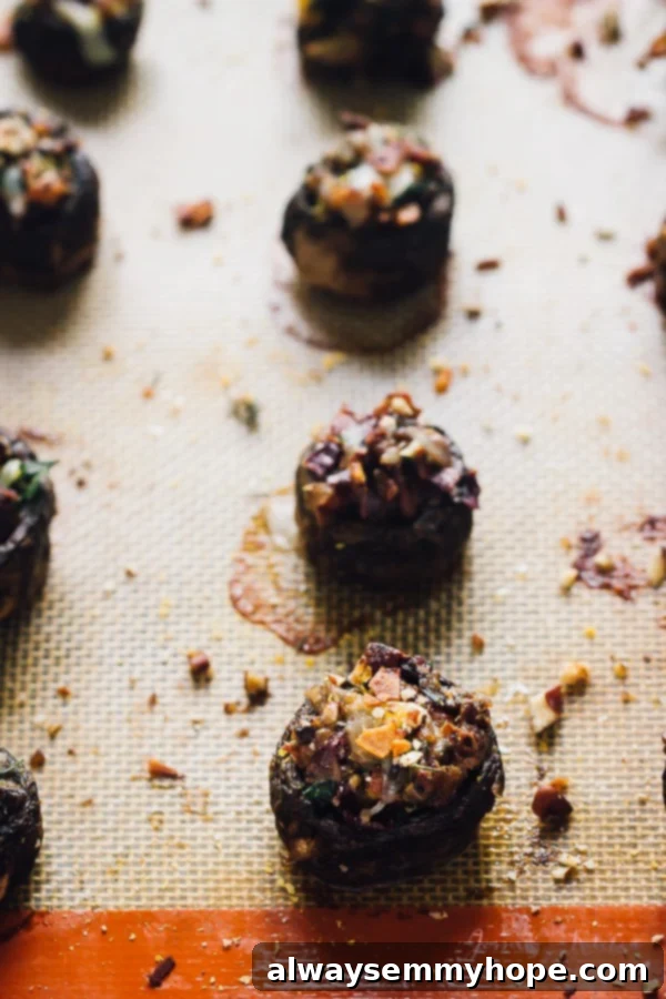 Close up of freshly baked stuffed mushrooms with coconut bacon on a silpat, featuring bubbling cheese and scattered nuts.