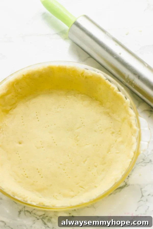 Unbaked gluten-free vegan pie crust in a glass pie plate, with a rolling pin and parchment paper in the background.