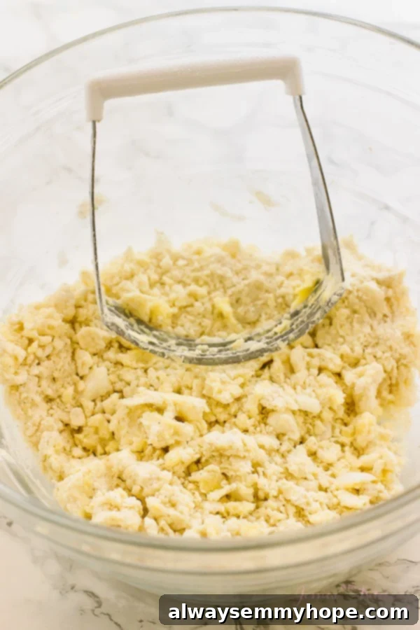 A pastry cutter being used in a large glass mixing bowl to combine gluten-free vegan pie crust dough ingredients.