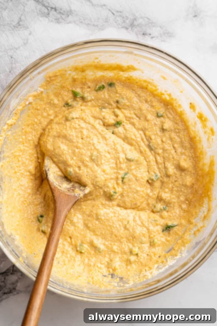 These moist vegan jalapeño cornbread muffins are easy to make and have a gluten-free option, which means everyone can enjoy them! Batter for cornbread muffins with jalapenos in bowl with wooden spoon.