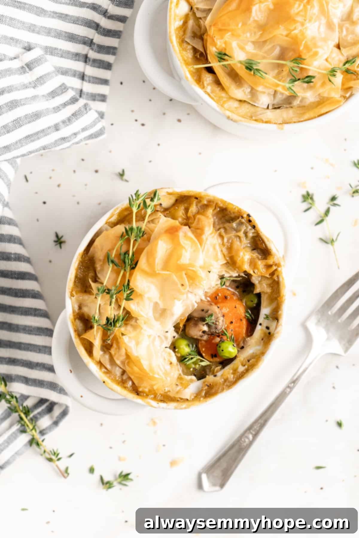 The Best Vegan Pot Pie – Easy, 1-Hour Recipe! Close-up top view of a vegan pot pie in a white ramekin with a portion of the crust gently pulled back to reveal the rich, creamy vegetable filling.