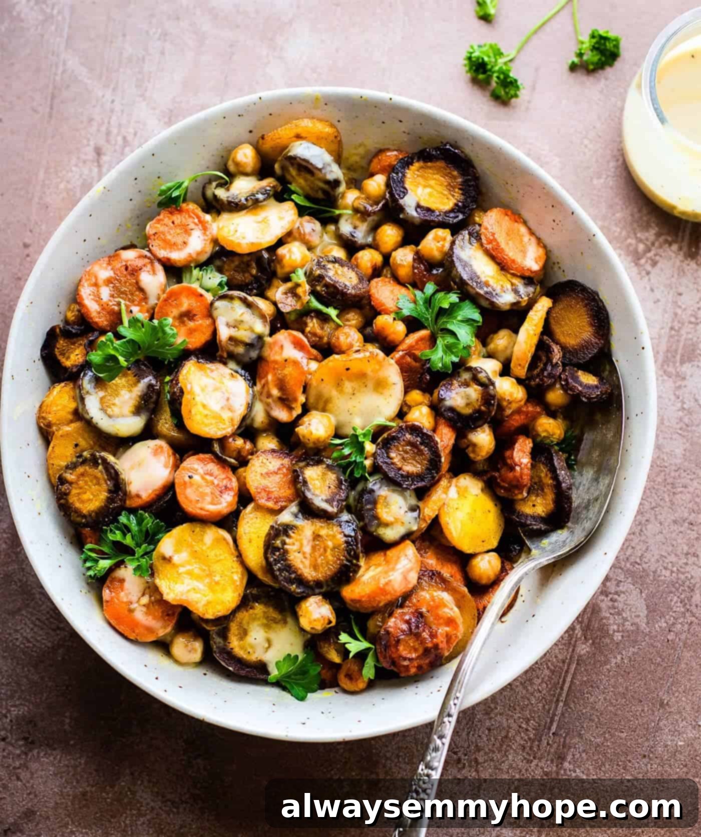 Top down shot of turmeric roasted carrot chickpea salad in a white bowl with a fork on the side. 