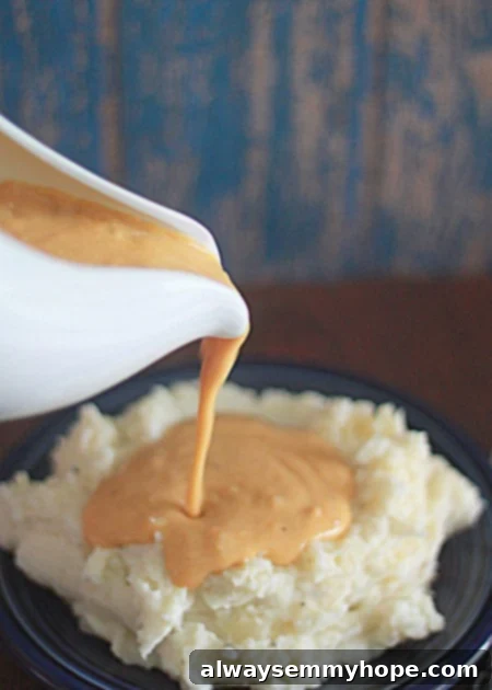 A gravy boat pouring out vegetarian onion gravy onto mashed potatoes. 