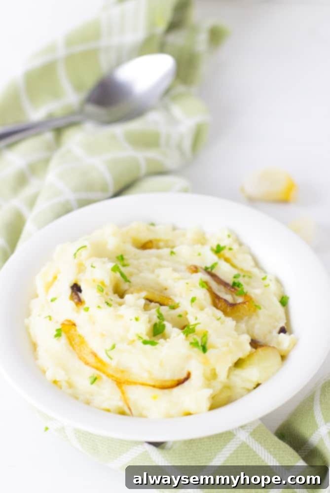 Best garlic mashed potatoes with caramelised onions in a white bowl with a spoon on the side. 