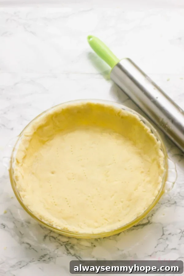 Vegan pie crust on a glass dish with a rolling pin on the side. 