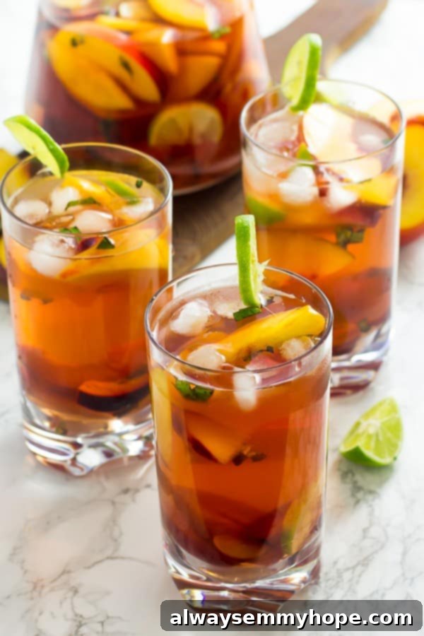 Three glasses of stone fruit sangria in front of a pitcher of sangria. 