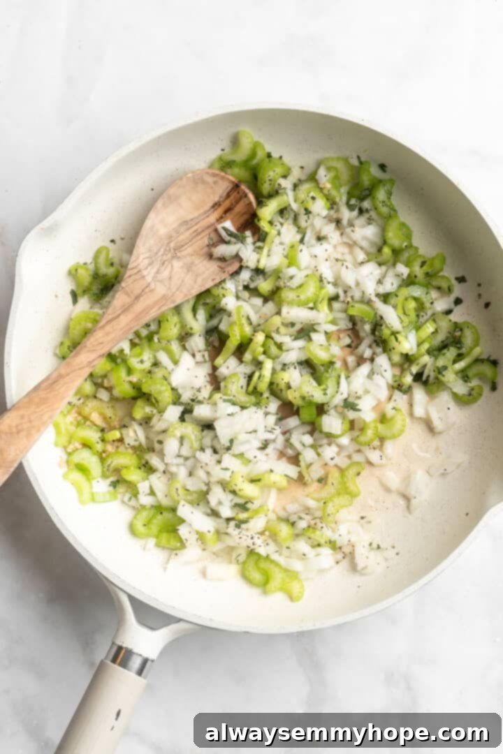 Overhead view of chopped celery, onion, and fresh herbs in a hot skillet, ready to be sautéed