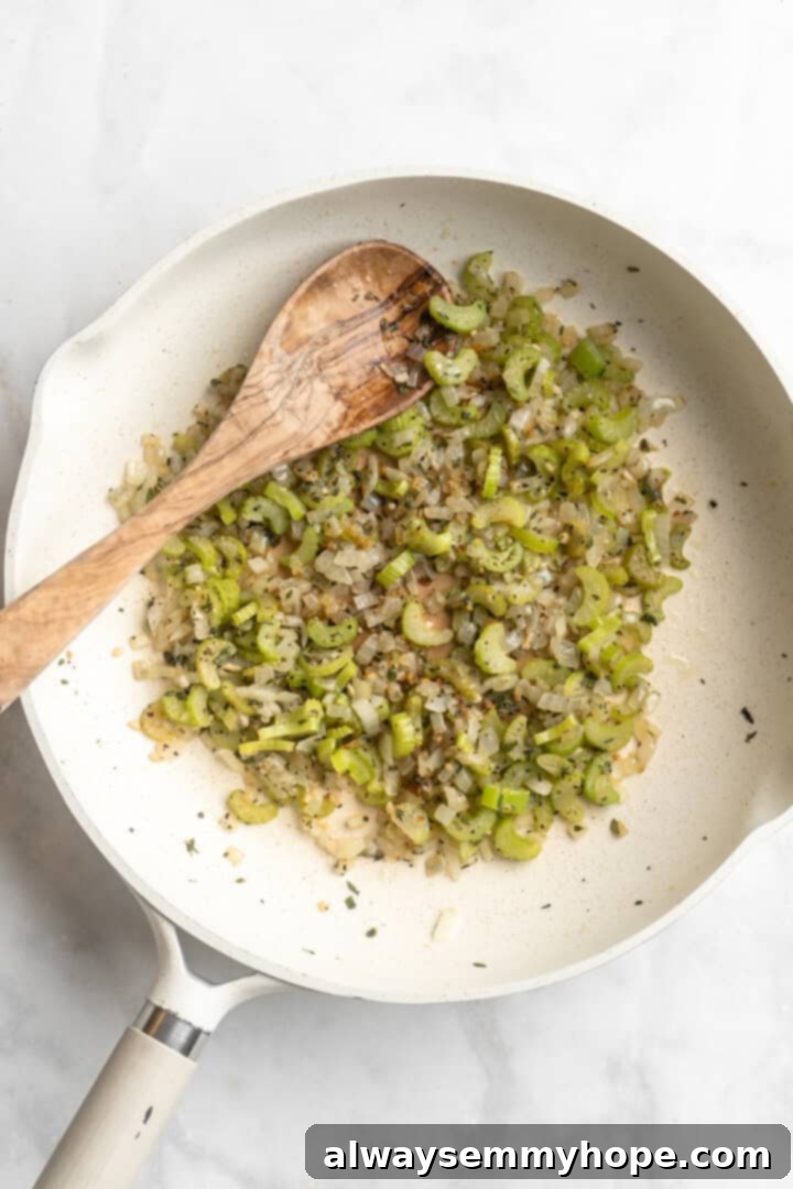 Overhead view of celery, onions, and fresh herbs gently cooking in coconut oil in a skillet, filling the kitchen with fragrant aromas